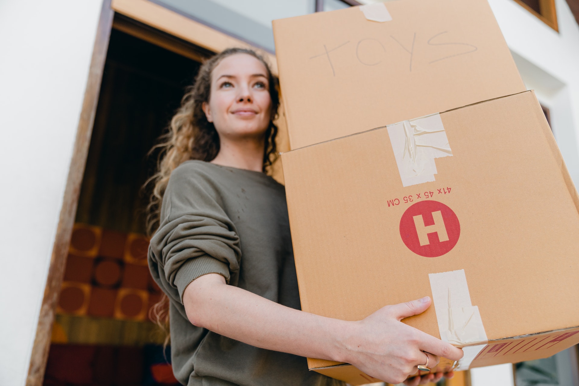A woman happily carrying two cardboard boxes while moving somewhere new.