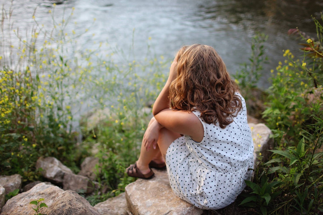 A woman sitting on a rock near a body of water.