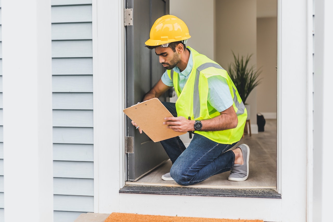 A man wearing a hard hat and yellow vest inspects a house door.