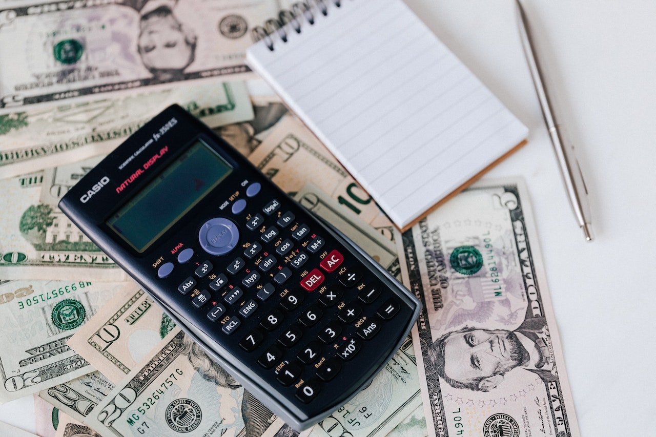 A calculator and a notepad on top of various dollar bills.