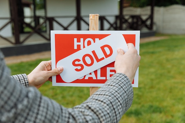 A person putting a sold sign over a house for sale sign.