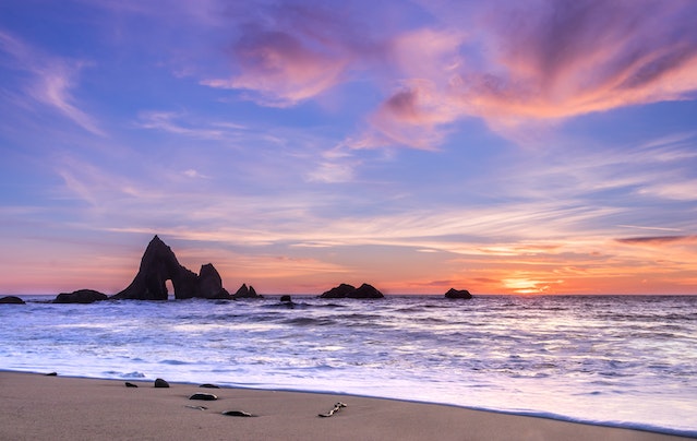 Sea and rock formation under the rose and orange sunset sky.