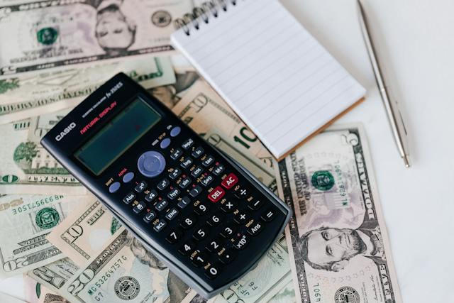: A calculator, a pen and a notebook on a pile of money.
