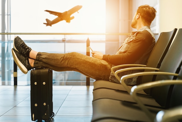 Man sitting at the airport with his legs lifted on a suitcase.