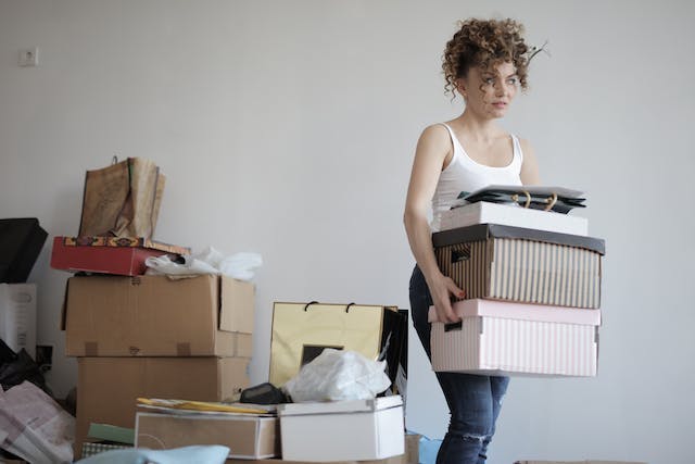 A woman holding stacked colorful boxes next to a pile of clutter.