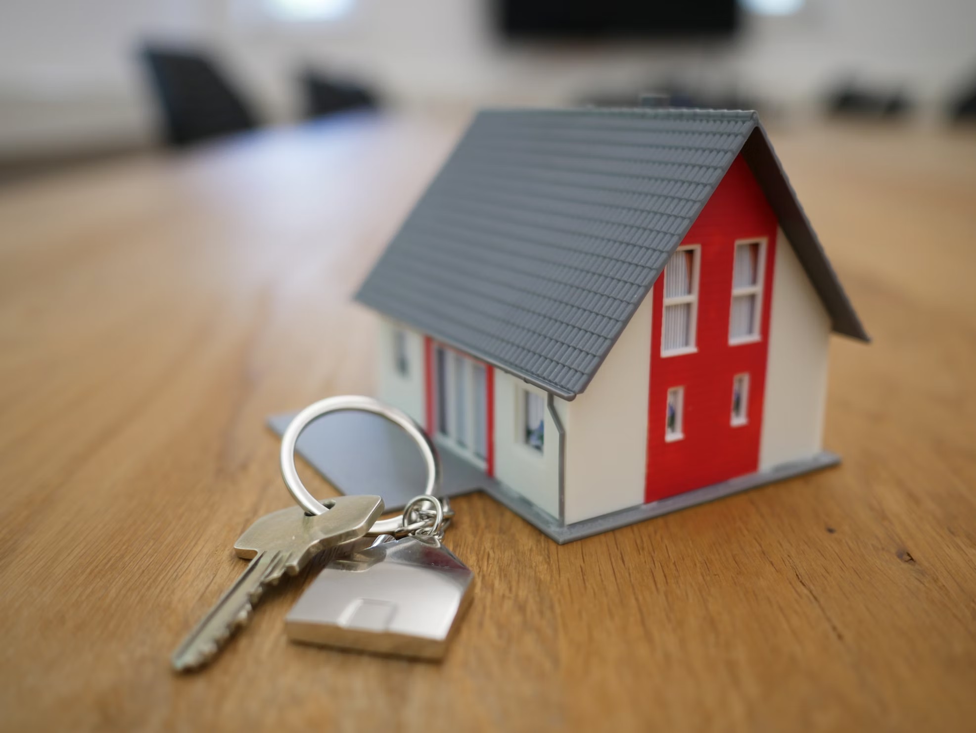 A miniature house next to a key on a wooden surface.