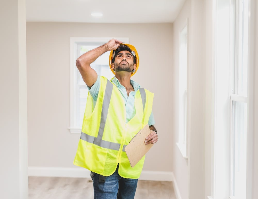 A man in a yellow vest inspecting a home’s interior.