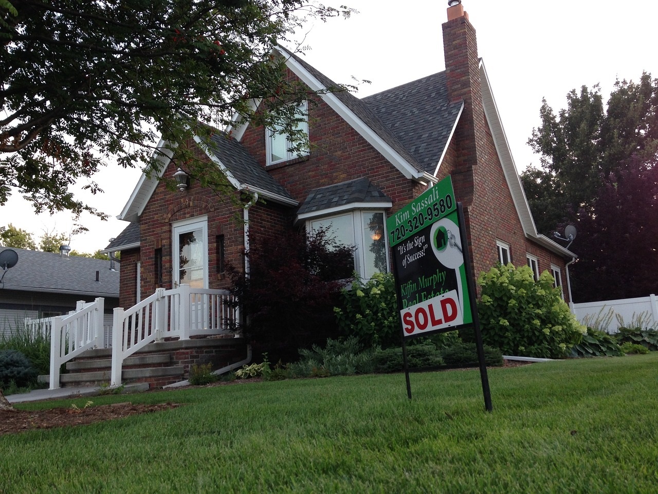 A brick house with a sold sign on its lawn.