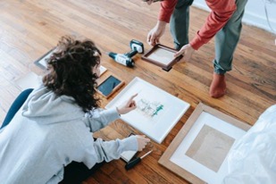 Two people sitting on the floor looking at a photo album with moving boxes around